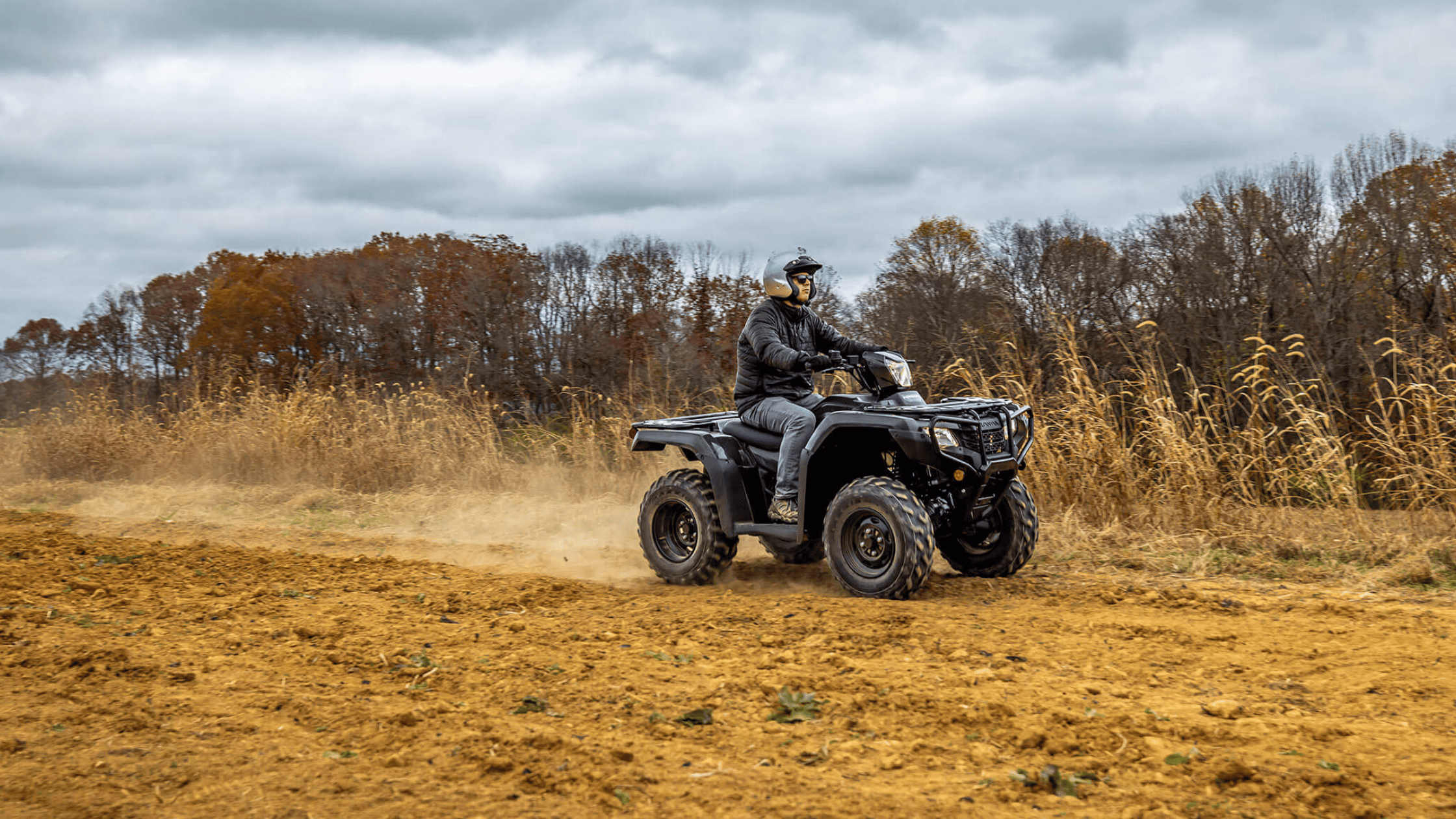 Rider on a black 2025 Honda FourTrax Foreman 4x4 ATV kicking up dirt on a fall trail