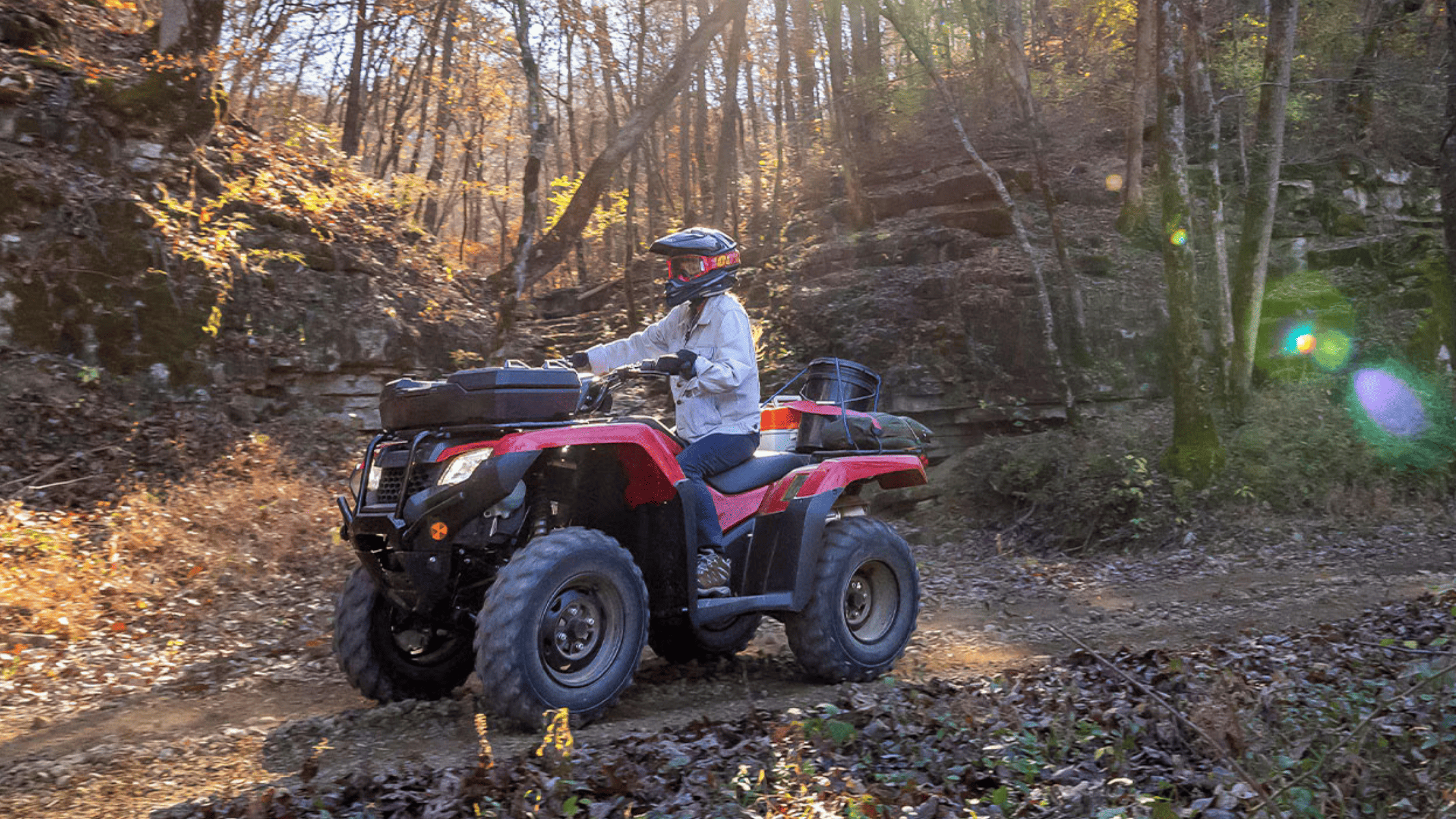 Red Honda FourTrax Rancher 4x4 ATV on forest trail, rider in helmet, side angle action shot