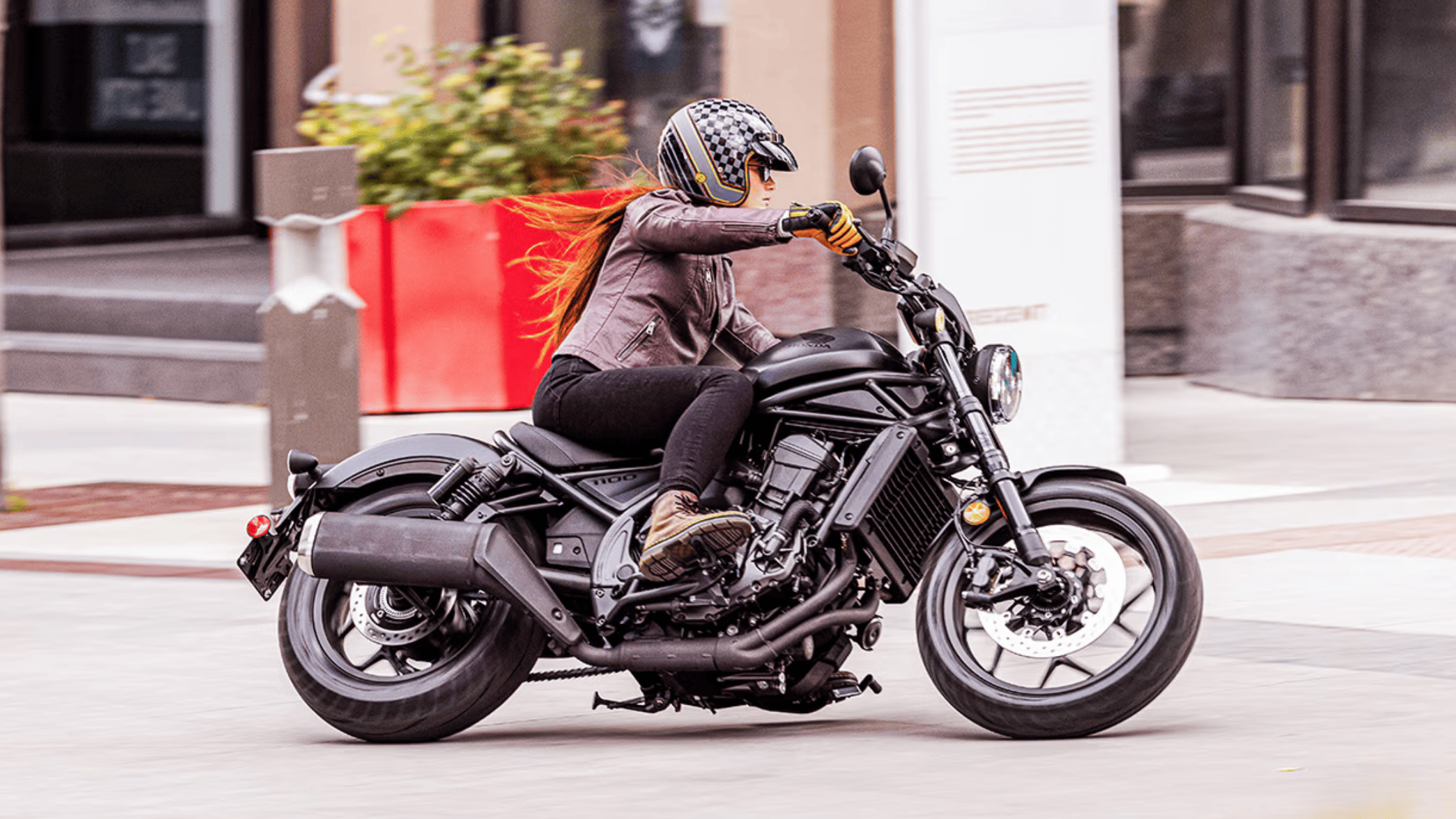 Motorcyclist riding blue 2025 Honda Rebel 500 on city street with palm trees in background