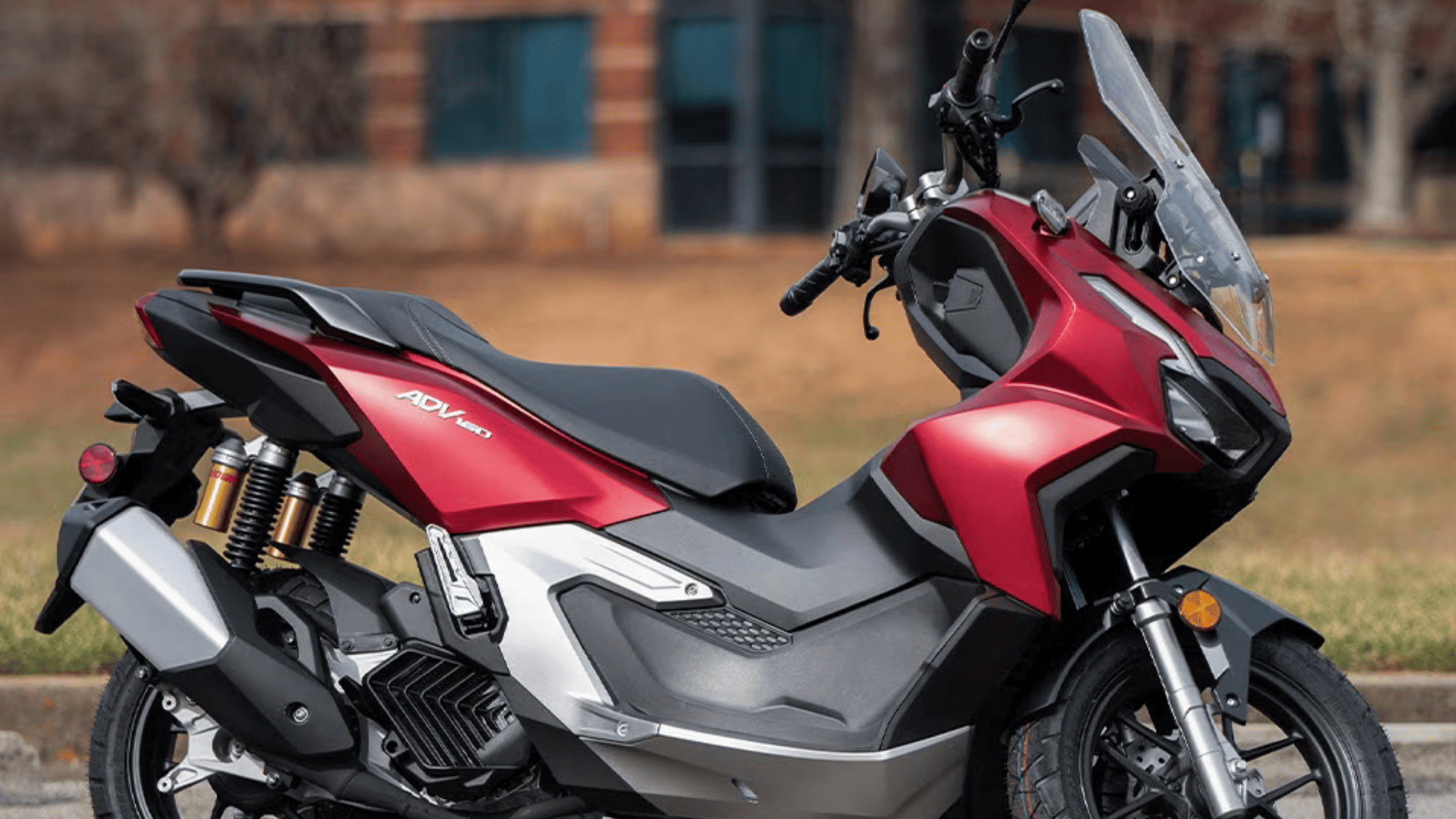 Red 2026 Honda ADV160 scooter side view showcasing adventure styling and windshield design.