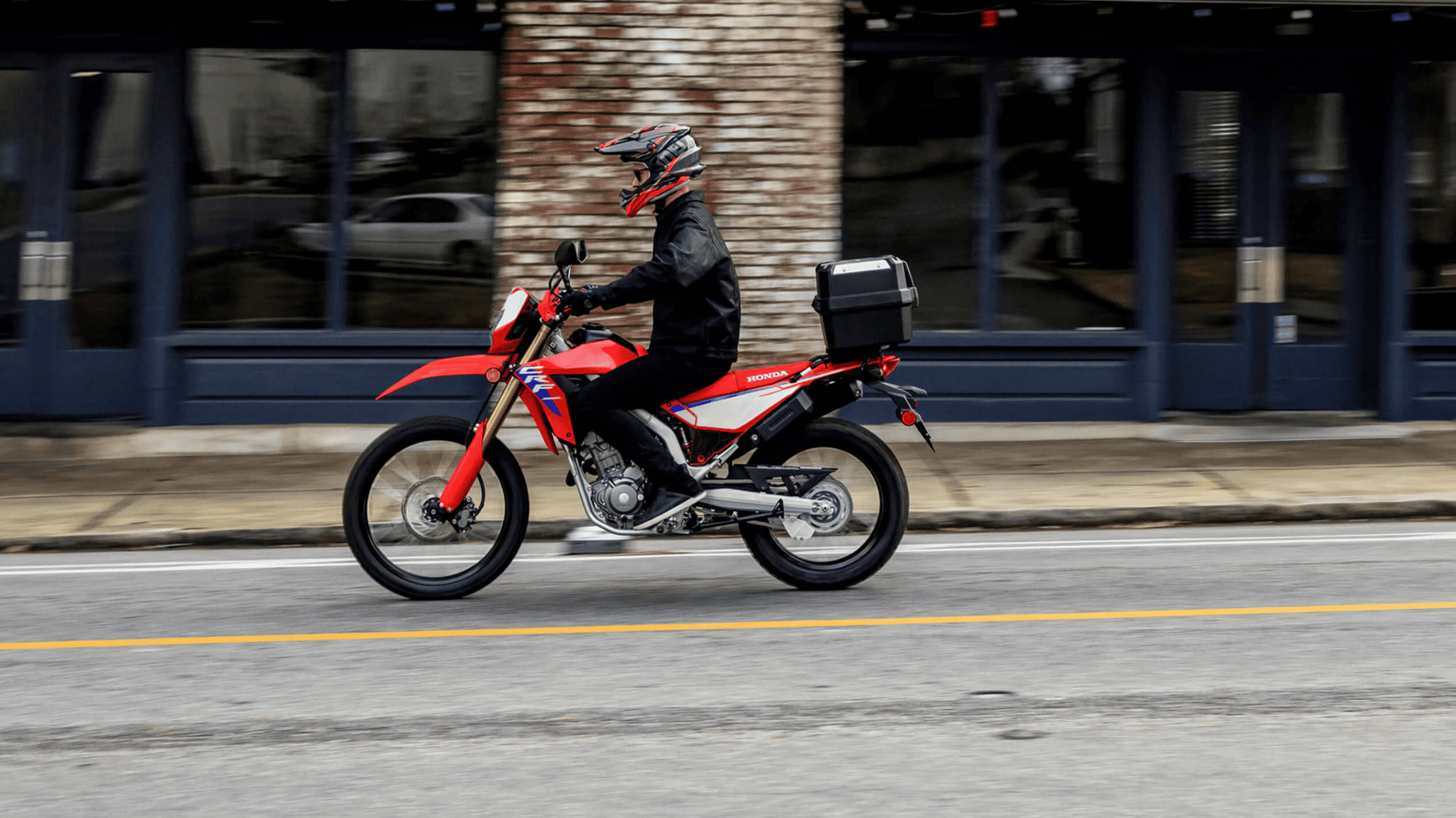 Red Honda CRF300L ABS motorcycle on city street, rider in helmet, side profile