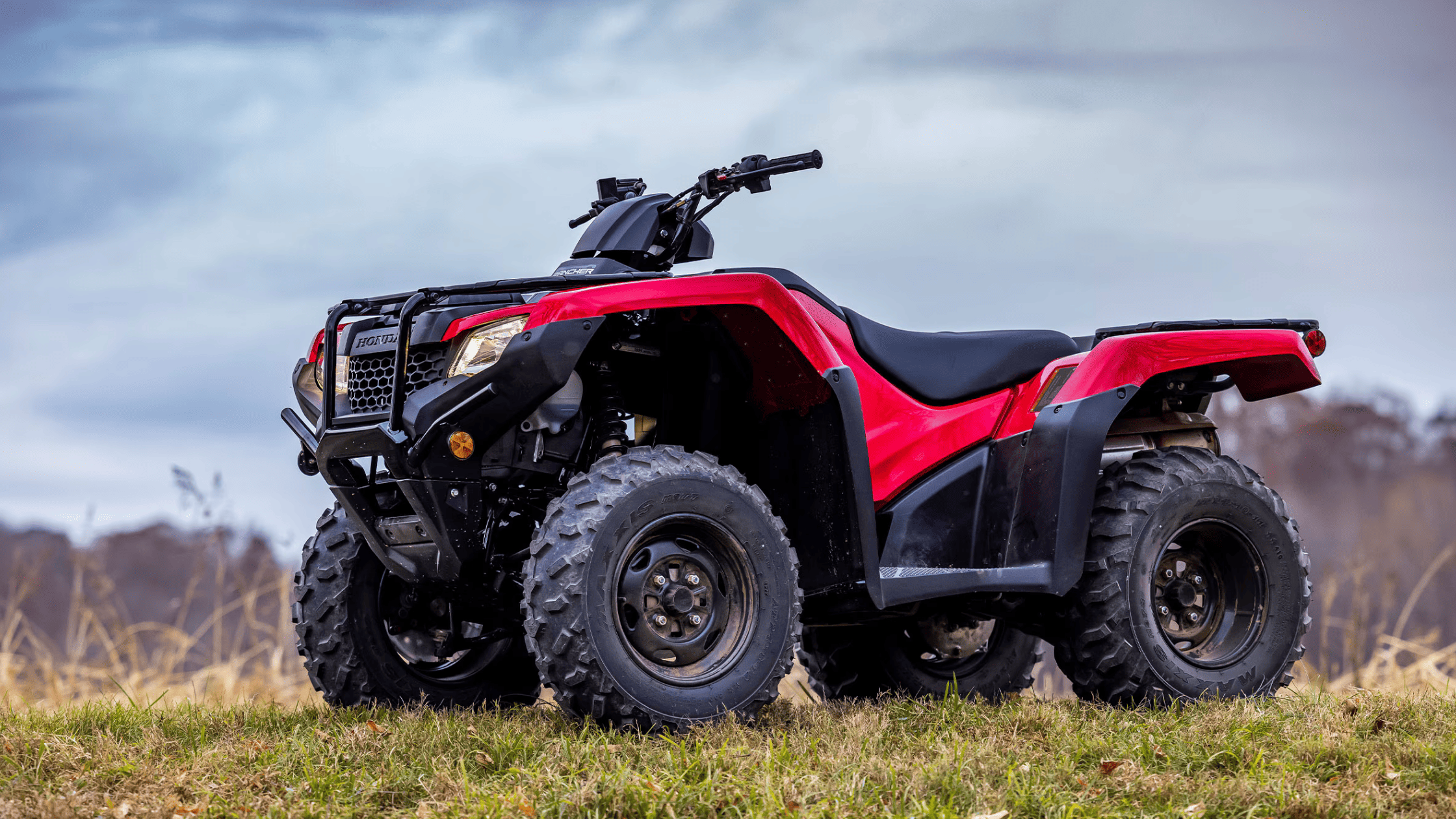 Red Honda FourTrax Rancher 4x4 ATV parked on grassy field, low-angle exterior view