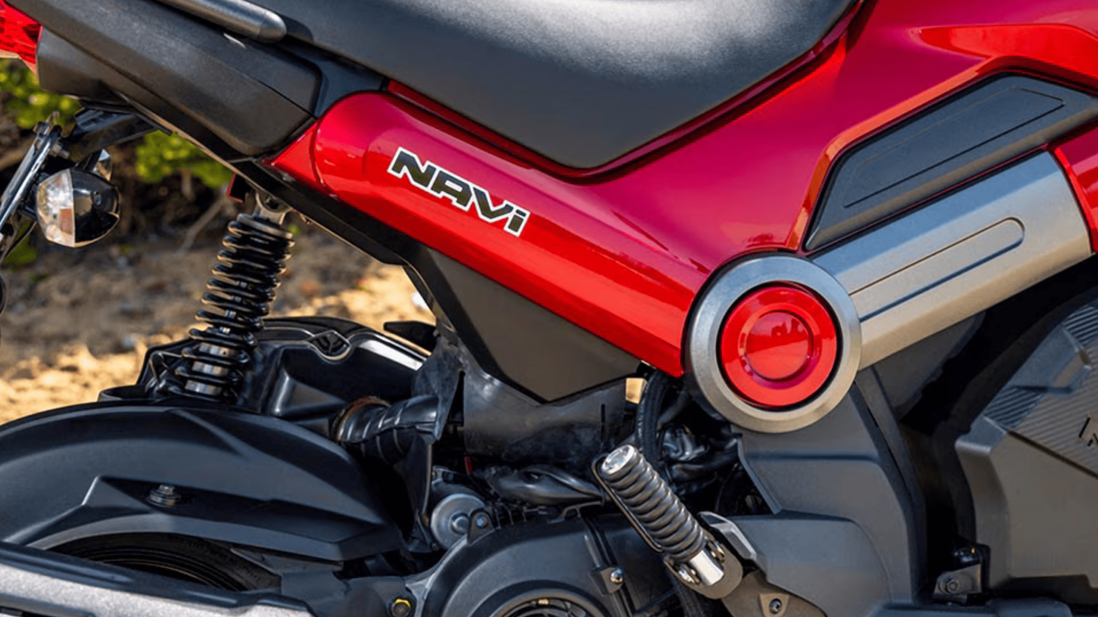 Close-up of the 2025 Honda Navi rear frame and suspension showing red bodywork and black seat design.