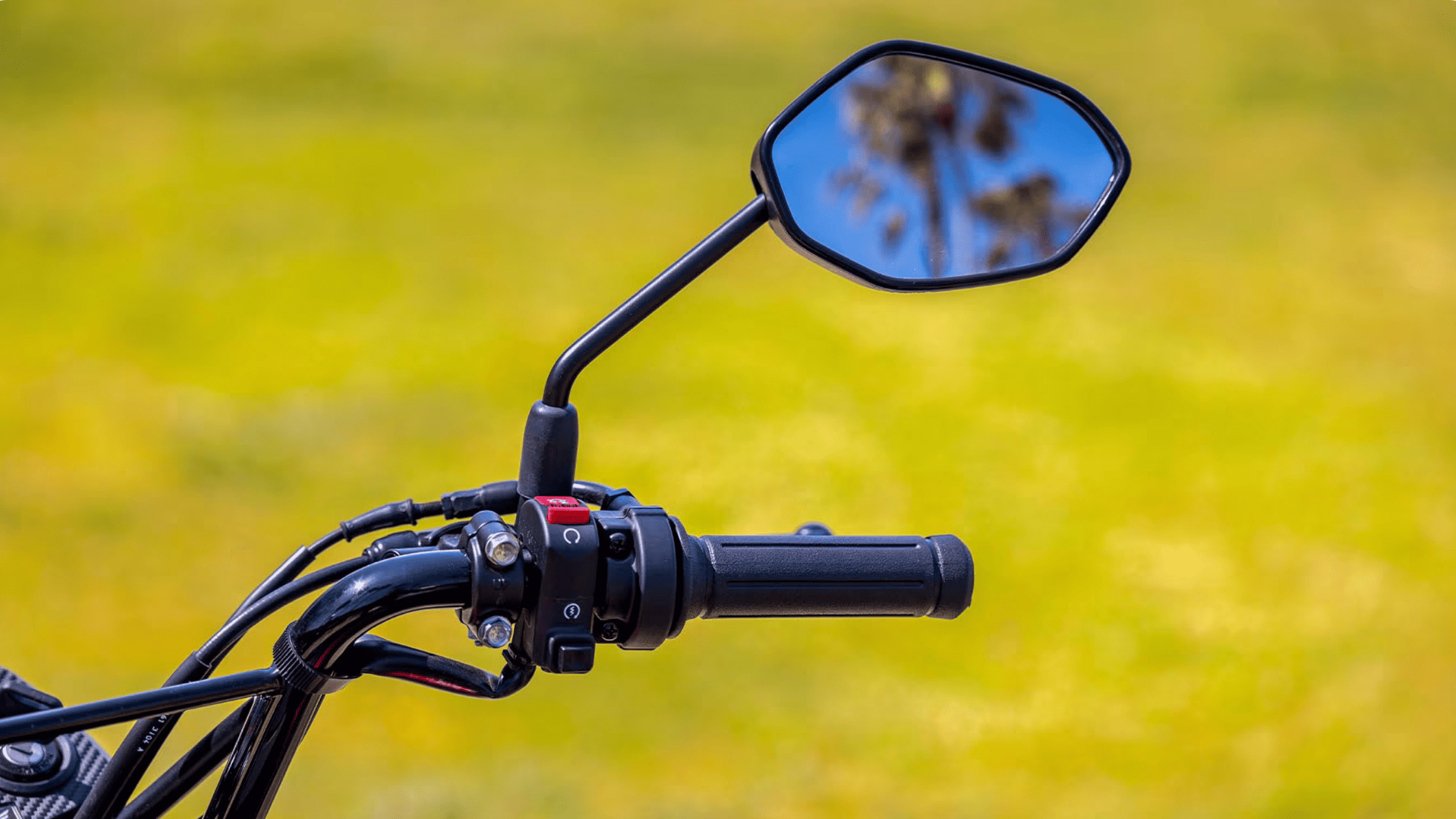 Handlebar and mirror view of the 2025 Honda Navi reflecting clear sky and palm trees in the background.