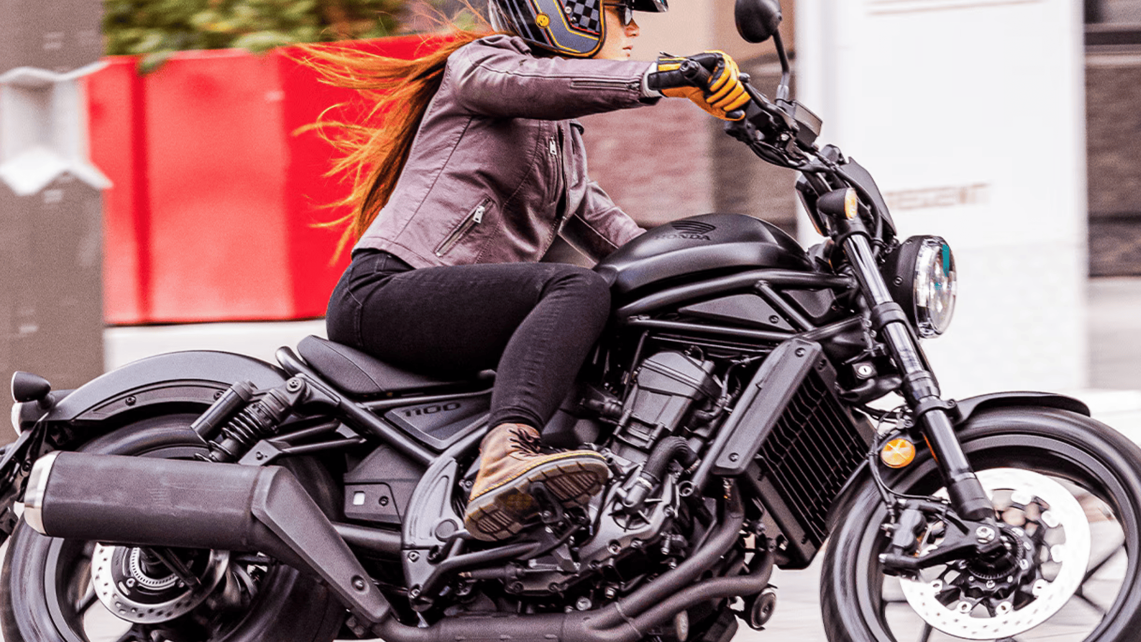 Rider sitting on red 2025 Honda Rebel 1100 DCT SE in urban setting, framed by modern glass buildings