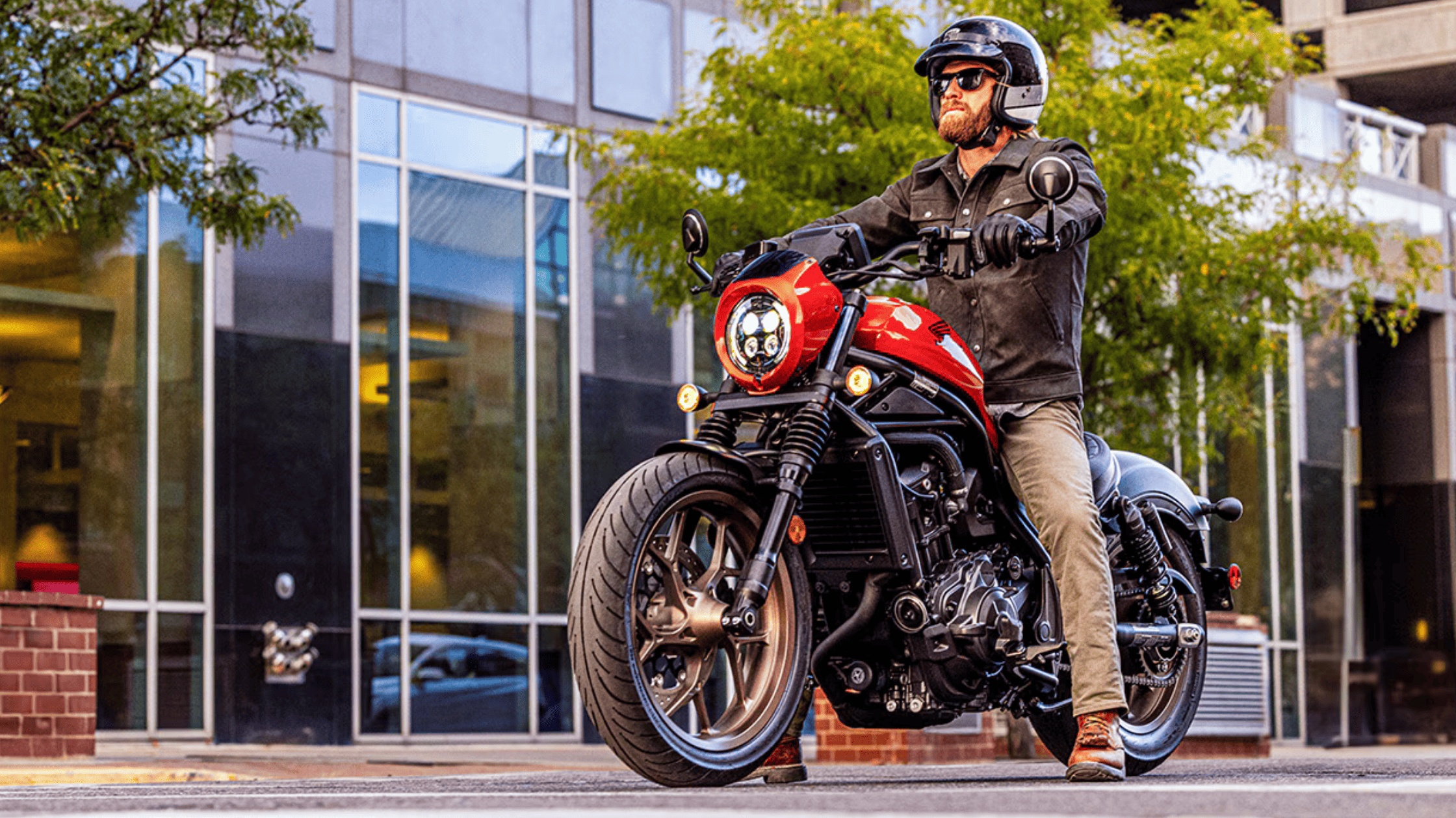 Matte black and red 2025 Honda Rebel 1100 DCT SE motorcycles parked side-by-side on city sidewalk