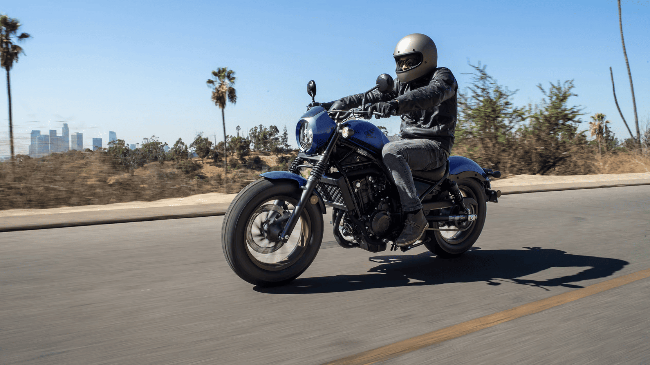 2025 Honda Rebel 500 in matte blue parked in front of a custom bike garage with classic tools and equipment