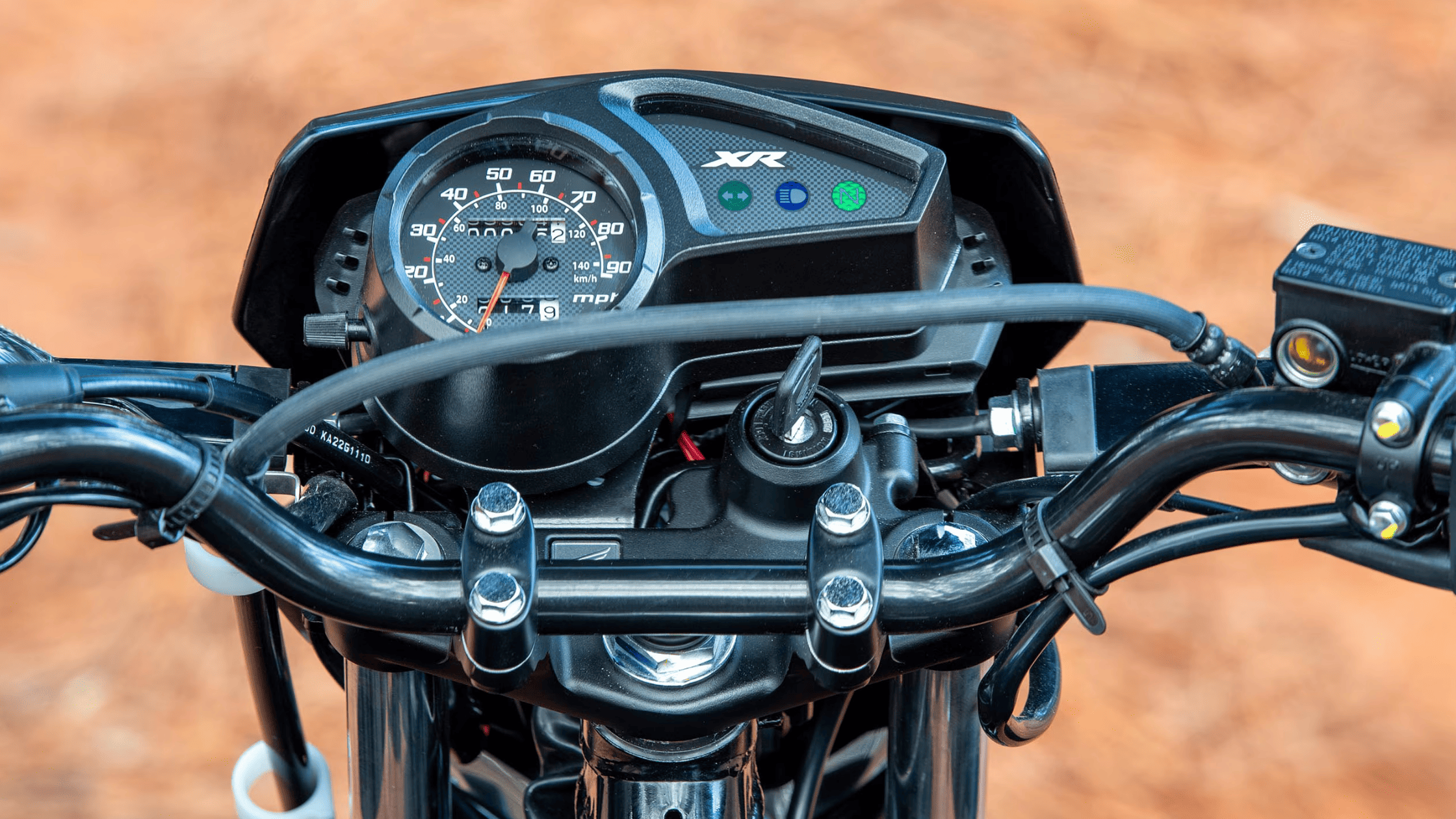 Dashboard close-up of Honda XR150L, speedometer and control panel with black handlebars