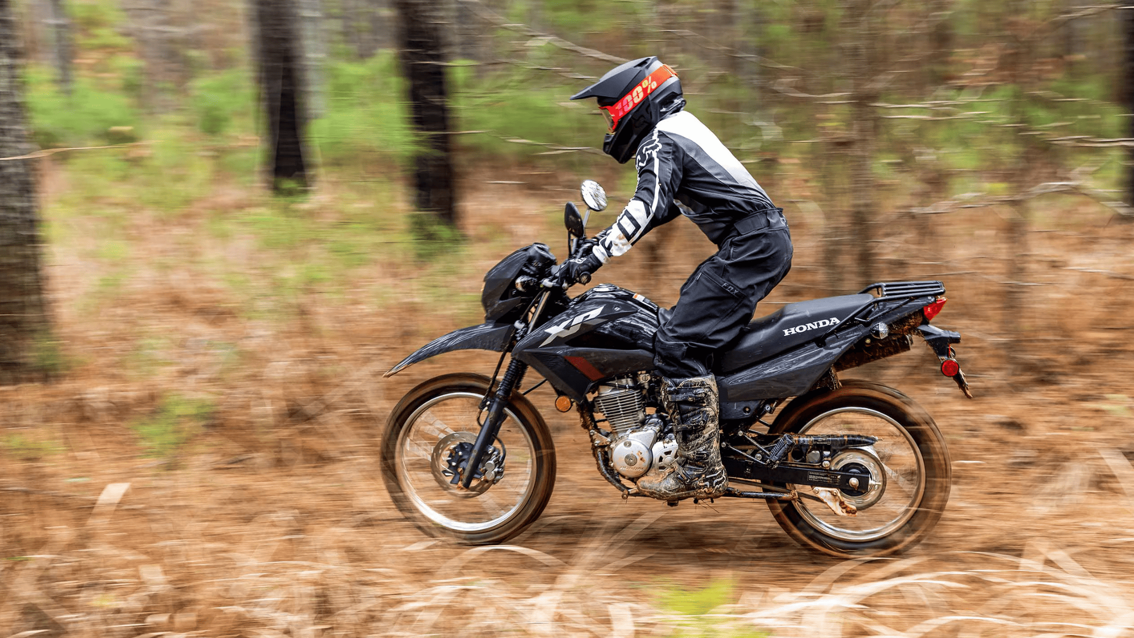 Black Honda XR150L motorcycle in forest trail, rider in helmet, side action shot